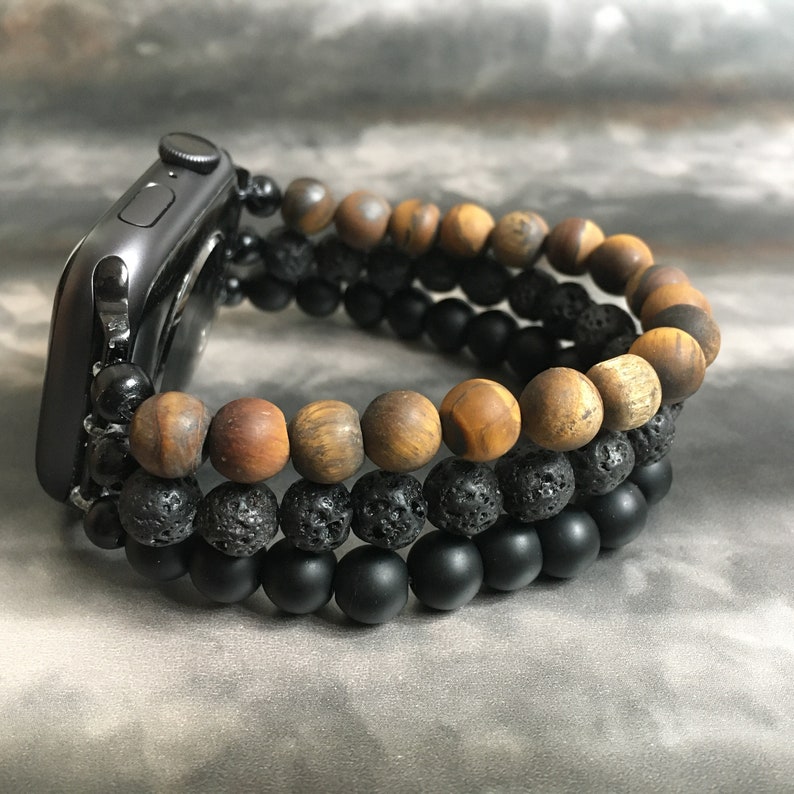 May include: A black Apple Watch with a brown, black, and gray beaded bracelet. The bracelet is made of tiger's eye, lava rock, and onyx beads.