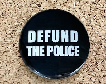 May include: Black and white button with the text "DEFUND THE POLICE" in white letters.