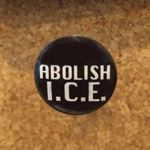 May include: A black button with white text that reads "ABOLISH I.C.E."
