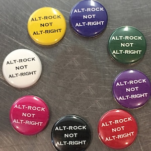 May include: Eight round buttons with the text "Alt-Rock Not Alt-Right" in black lettering on a white background. The buttons are in various colors: yellow, purple, green, white, pink, black, red, and purple.