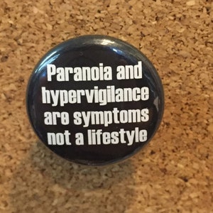 May include: Black button with white text that reads "Paranoia and hypervigilance are symptoms not a lifestyle."