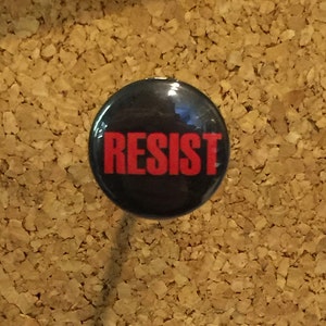 May include: A black button with the word "RESIST" in red letters.