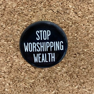 May include: A black button with white text that reads "STOP WORSHIPPING WEALTH".
