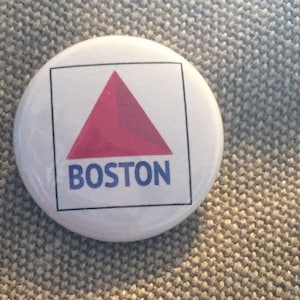 May include: A white button with a red triangle and the word "BOSTON" in blue letters.