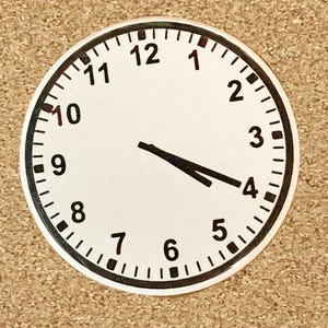 May include: A white analog clock face with black numbers and hands. The clock face is surrounded by a black circle with a white border. The time is 4:00.