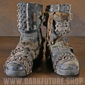 Op de afbeelding: Een paar zwarte laarzen met gestructureerde bandprofielpanelen op de schachten, metalen kettingen met puntige studs over de neuzen en gerafelde stoffen banden. De tekst WWW.DARKFUTURE.SHOP staat in het wit onderaan de afbeelding gedrukt.