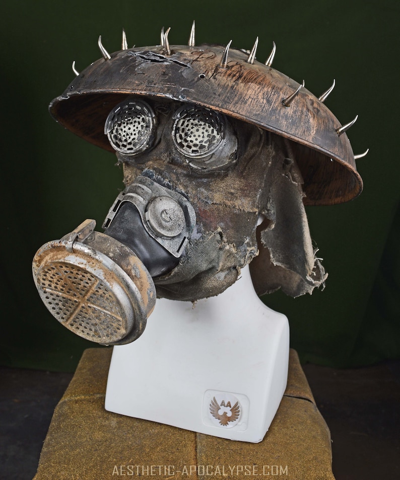 May include: A brown, weathered gas mask with a metal helmet and spikes. The mask has a black rubber mouthpiece and a filter on the side. The helmet has two round, metal eye pieces.