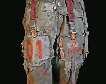 May include: Distressed olive green pants with patches, red accents, and suspenders. The pants feature the numbers "01" and "77 JACKAL" painted in red. The design includes a black belt and leather details, creating a rugged, post-apocalyptic aesthetic.
