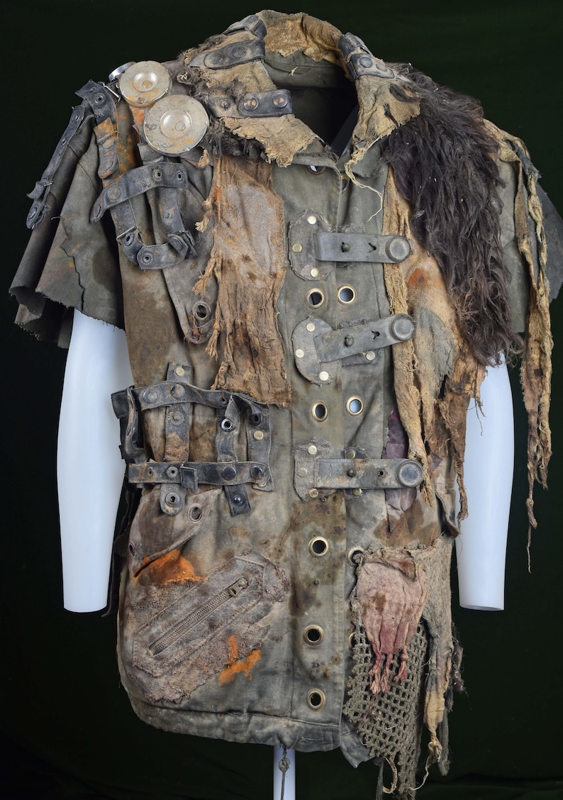 K&ouml;nnte beinhalten: Ein braunes und gr&uuml;nes, stark abgenutztes, mehrschichtiges und geflicktes Hemd mit einem Pelzkragen und mehreren Riemen und Schnallen.