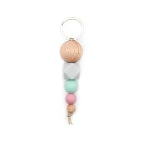 Könnte beinhalten: Ein Schlüsselanhänger aus Holzperlen mit einem silbernen Ring, einer grauen Silikonperle, einer hellblauen Silikonperle, einer rosa Silikonperle und einer braunen Schnur.