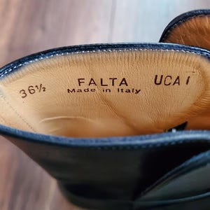 May include: Close-up of the inside of a black leather boot. The boot's interior is tan with the text "FALTA Made in Italy" and the size "36 1/2" printed on the leather.