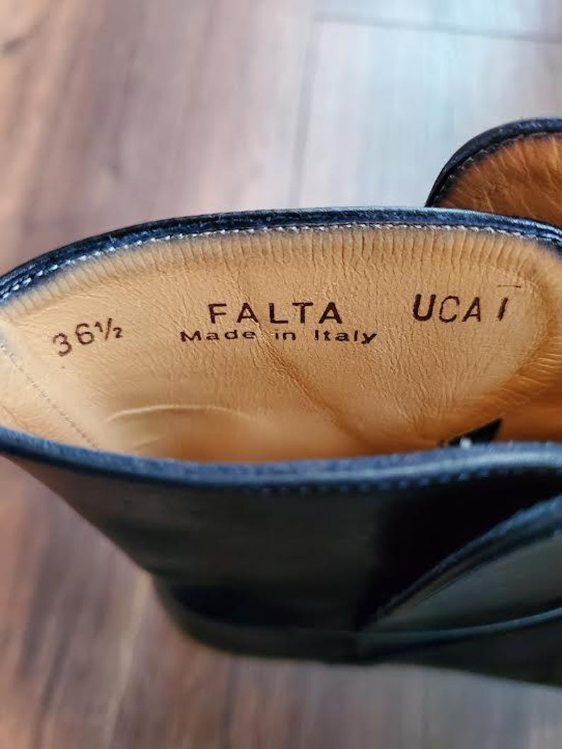 May include: Close-up of the inside of a black leather boot. The boot's interior is tan with the text "FALTA Made in Italy" and the size "36 1/2" printed on the leather.