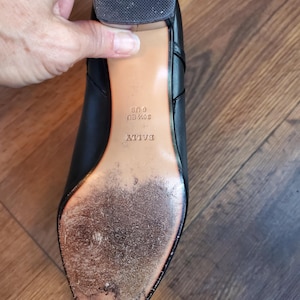 May include: Black leather shoe with a worn sole. The shoe has a block heel and the brand name "BALLY" is visible. The sole shows signs of wear and tear, indicating previous use. The shoe size is US 6 and EU 36 1/2.