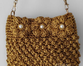 May include: A small, crocheted handbag with a gold chain strap. The bag is brown and has three white pearl embellishments on the front.