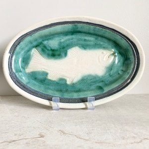 May include: A white ceramic oval serving dish with a raised fish design. The dish is glazed in a green and blue color.