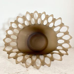 May include: A brown glass bowl with a scalloped edge and a lace-like design. The bowl is made of frosted glass and has a delicate, feminine look.
