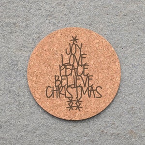May include: A round cork coaster with a brown Christmas tree design. The tree is made up of the words "Joy", "Love", "Peace", "Believe", and "Christmas".