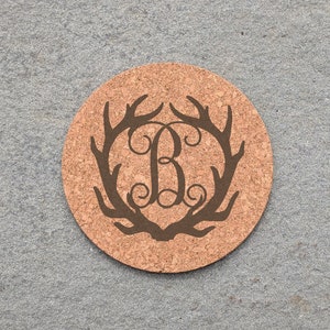 May include: A round cork coaster with a brown antler design and the letter "B" in a decorative font in the center.