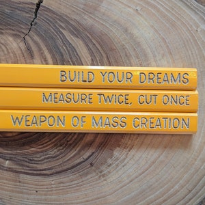 May include: Three yellow pencils with the text "BUILD YOUR DREAMS", "MEASURE TWICE, CUT ONCE", and "WEAPON OF MASS CREATION" printed on them.