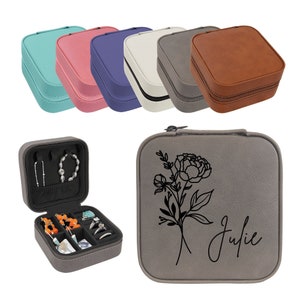 May include: A gray faux leather jewelry box with a floral design and the name "Julie" engraved on the front. The box is open to reveal a black velvet interior with compartments for rings, earrings, and a necklace.