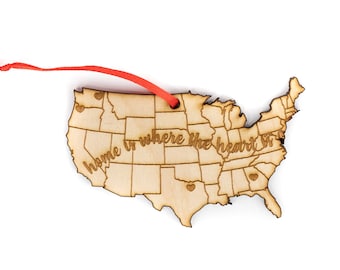 May include: A wooden ornament shaped like the United States of America with the text "Home is where the heart is" and small hearts marking different states. The ornament is attached to a red ribbon.