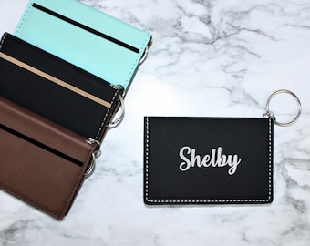 May include: Four leather card holders with key rings. The card holders are in brown, black, and light blue. One card holder is black with the name "Shelby" embossed in silver.