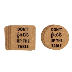 May include: A stack of square and round cork coasters. Each coaster has the phrase "DON'T fuck UP THE TABLE" printed in black, stylized font. The coasters are a natural, light brown color.