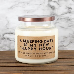 K&ouml;nnte beinhalten: Eine Glas-Kerze in einem Glas mit einem Kupferdeckel und einem braunen Papieretikett mit der Aufschrift "A Sleeping Baby Is My New "Happy Hour"" 16.5 oz Hand Poured Soy Candle -Baum Designs-