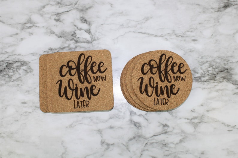 May include: Two cork coasters with the text "coffee now wine later" in black script. One coaster is square and the other is round.