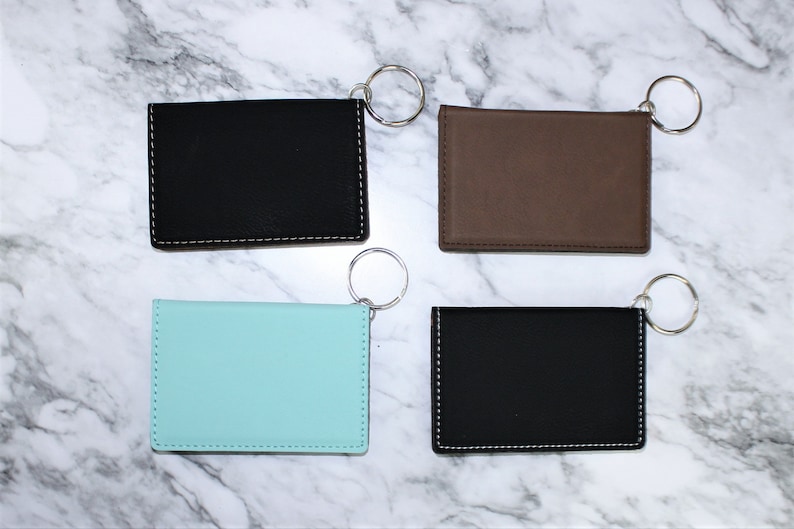 May include: Four keychains with different colored leather card holders. The keychains are silver and the card holders are black, brown, light blue, and black.
