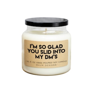 May include: A white soy candle in a clear glass jar with a black lid. The candle has a brown paper label with the text "I'M SO GLAD YOU SLID INTO MY DM'S" and "16.5 OZ HAND POURED SOY CANDLE -BAUM DESIGNS-"