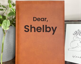 May include: A brown leather-bound journal with the text "Dear, Shelby letters to my daughter" on the front cover.