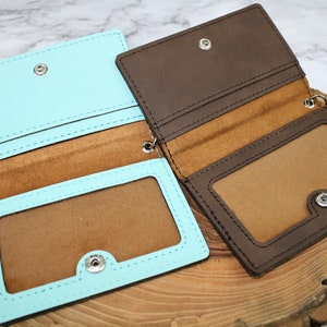 May include: Two leather card holders, one in brown and one in light blue, with a clear plastic window for ID cards. Both have a snap closure and a key ring.