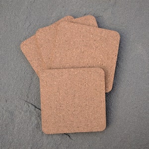 May include: Four brown cork coasters stacked on top of each other on a gray textured surface.