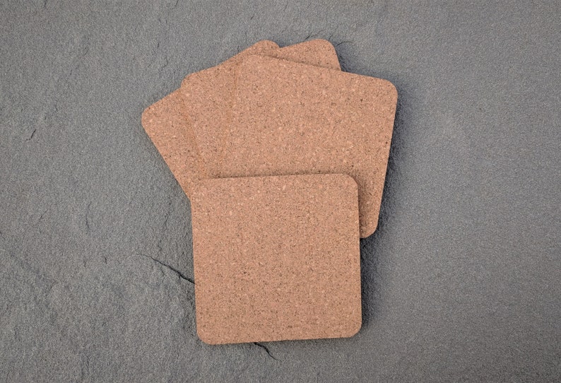 May include: Four brown cork coasters stacked on top of each other on a gray textured surface.