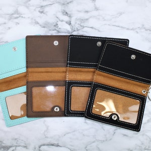 May include: Four different colored leather wallets with a clear plastic window and a metal ring. The wallets are brown, black, light blue, and dark blue.