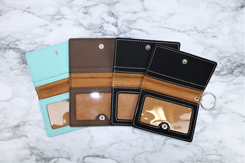 May include: Four different colored leather wallets with a clear plastic window and a metal ring. The wallets are brown, black, light blue, and dark blue.