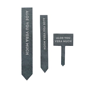 May include: Three slate plant markers with the text "Aloe You Vera Much" in white lettering. The markers are different sizes and shapes.