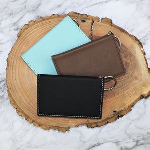 May include: Three leather card holders with key rings. The card holders are in black, brown, and light blue.
