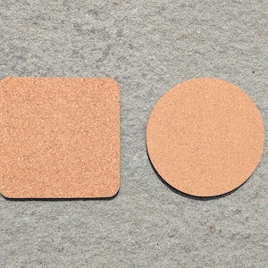 May include: Two cork coasters, one square and one round, on a gray textured surface.