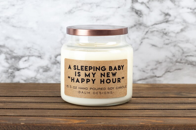 K&ouml;nnte beinhalten: Eine Glas-Kerze in einem Glas mit einem Kupferdeckel und einem braunen Papieretikett mit der Aufschrift "A sleeping baby is my new "happy hour"" 16.5 oz hand poured soy candle - Baum Designs -