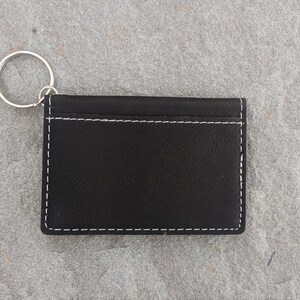 May include: Black leather key chain with a silver ring. The keychain has white stitching around the edges.