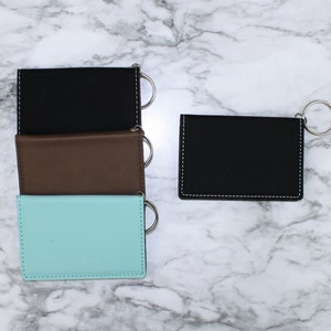 May include: Three leather keychains in black, brown, and light blue with silver key rings. The keychains are stacked on top of each other. A fourth black keychain with a silver key ring is to the right.