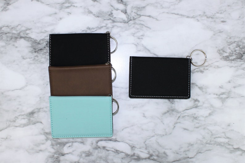 May include: Three leather keychains in black, brown, and light blue with silver key rings. The keychains are stacked on top of each other. A fourth black keychain with a silver key ring is to the right.