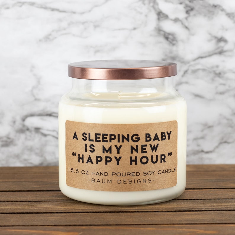 K&ouml;nnte beinhalten: Eine Glas-Kerze in einem Glas mit einem Kupferdeckel und einem braunen Papieretikett mit der Aufschrift "A Sleeping Baby Is My New "Happy Hour"" 16.5 oz Hand Poured Soy Candle -Baum Designs-