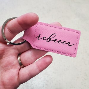 May include: Pink leather keychain with a silver key ring and the name "rebecca" written in black cursive.