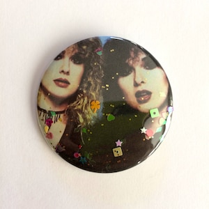 May include: A round button with a black background and a glittery finish. The button features a photo of two women with long hair. The photo is surrounded by colourful glitter.