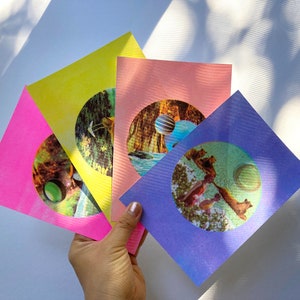 May include: Four colourful cards with circular images of nature scenes. The cards are pink, yellow, purple, and blue. Each card has a different image, including a forest, a lake, and a field.