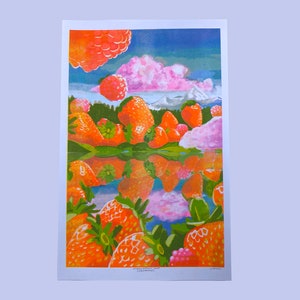 K&ouml;nnte beinhalten: Ein farbenfrohes Gem&auml;lde einer Landschaft mit einem See, der einen Himmel mit rosa Wolken und eine Bergkette im Hintergrund spiegelt. Der Vordergrund ist mit gro&szlig;en, orangen Erdbeeren gef&uuml;llt.