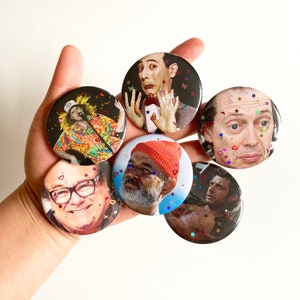 Puede incluir: Seis botones de colores con diferentes retratos de personas. Los botones son redondos y tienen un acabado brillante. Los retratos incluyen un hombre con un sombrero rojo, un hombre con bigote, un hombre con barba, un hombre con una camisa a rayas rojas y blancas, un hombre con una camisa azul y un hombre con una camisa negra.